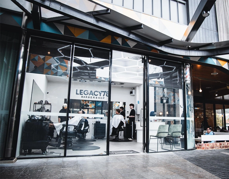 Exterior view of Legacy78 Barbershop in Perth, Australia, featuring a glass-fronted barber shop with visible barber chairs inside.